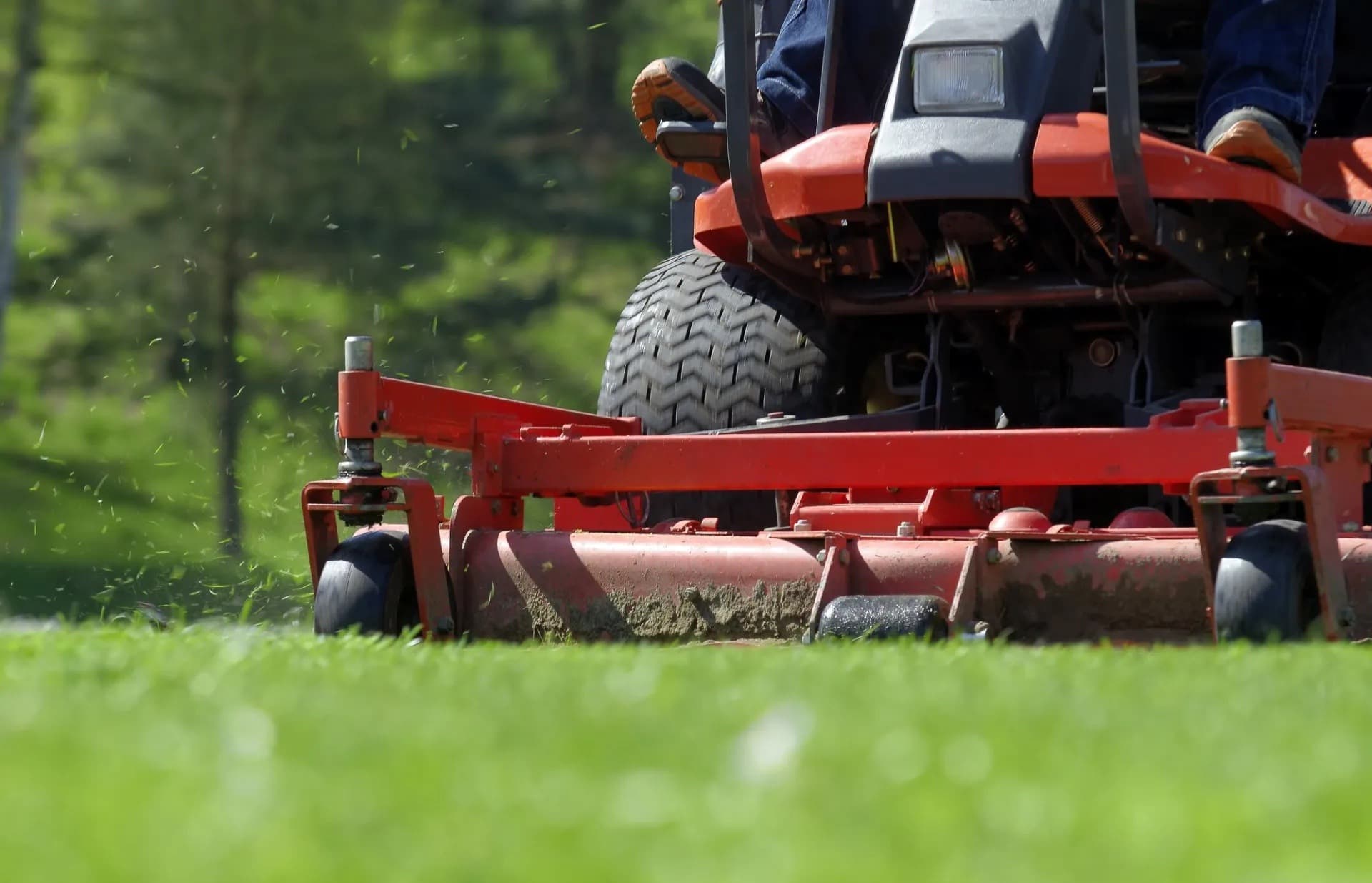 Close view of a red riding mower cutting green grass with clippings flying.
