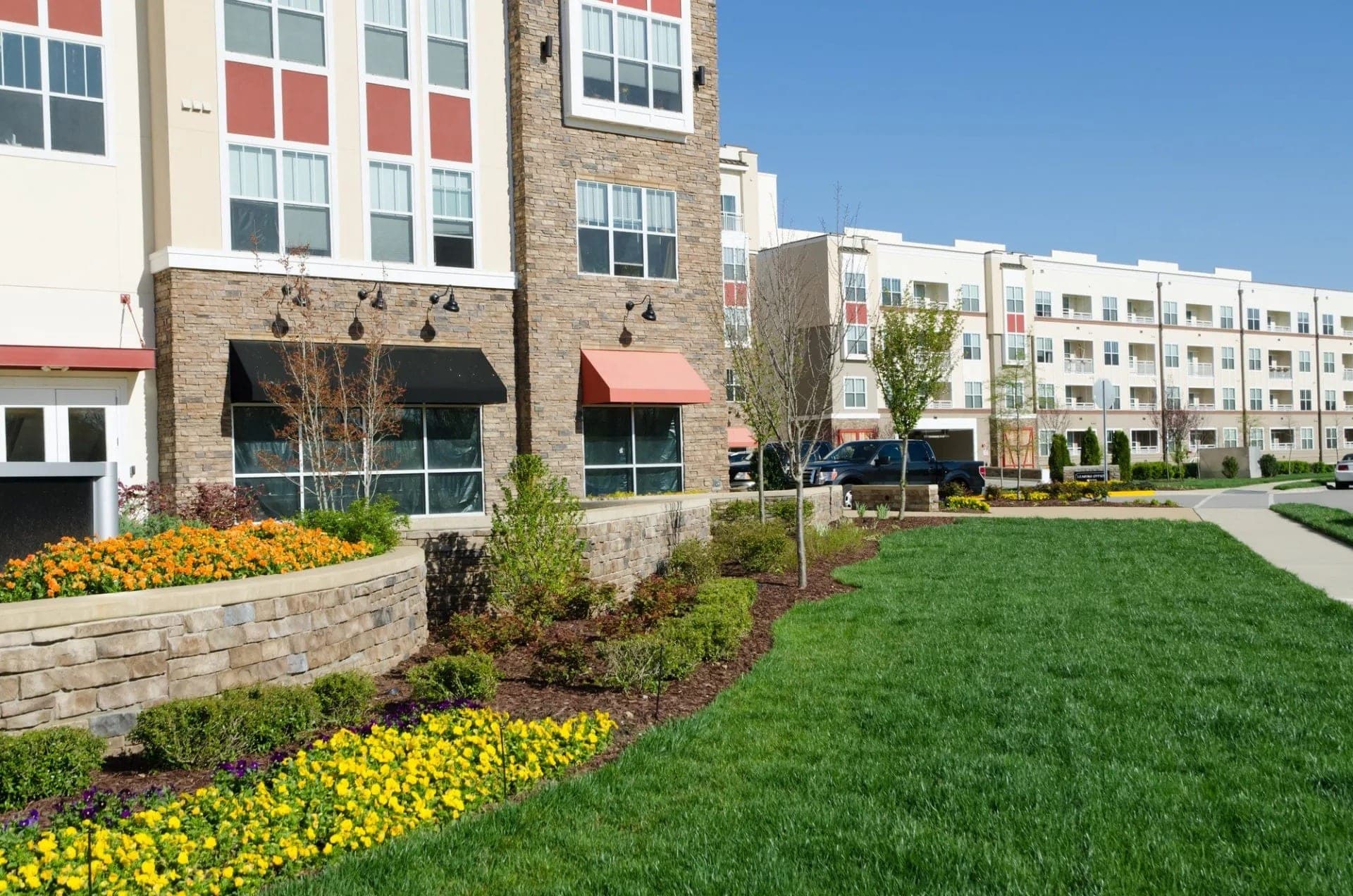Apartment complex frontage with stone planter walls, flower beds, mulch, and mowed lawn.